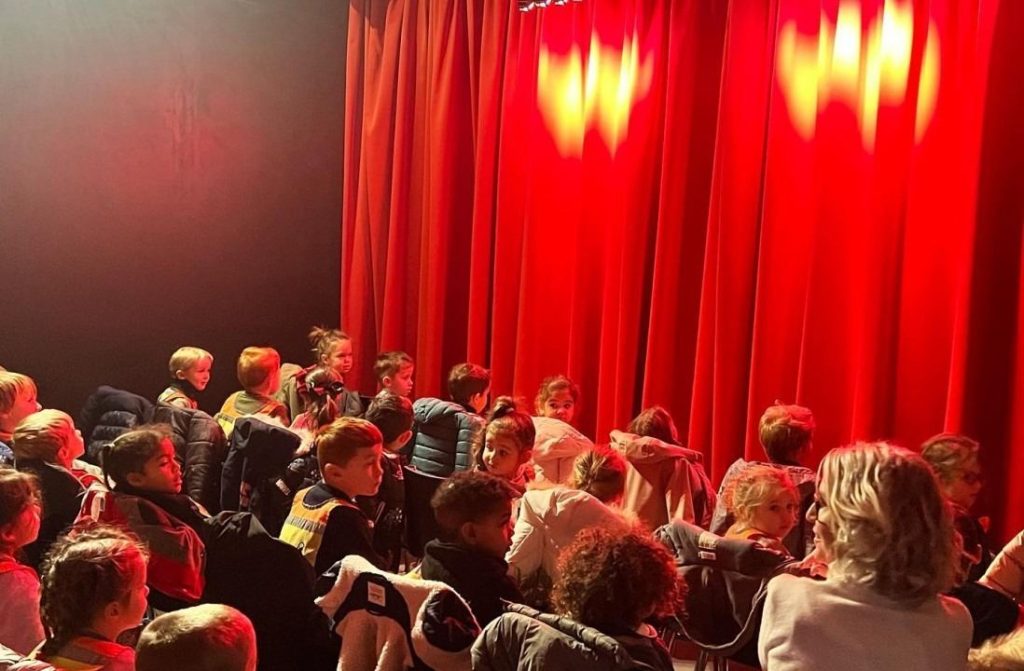 Enfants assis dans la salle devant le rideau rouge