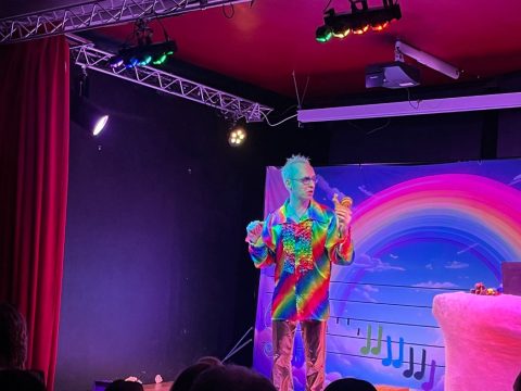 Comédien en chemise arc-en-ciel devant un décor de notes